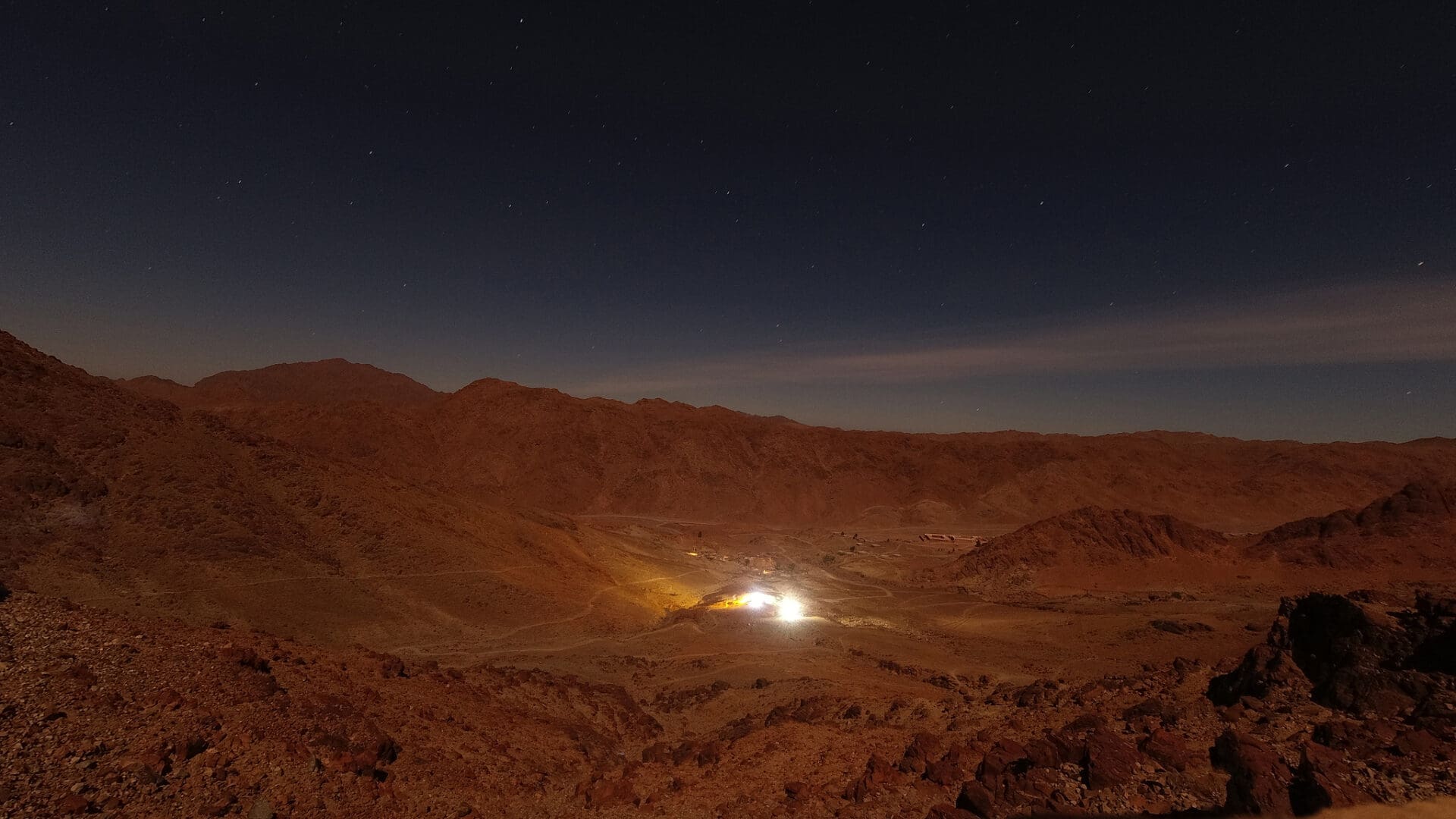 A light shines in the dark on top of a mountain.